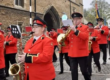 A marching band in bright red uniforms plays instruments whilst walking down a street.