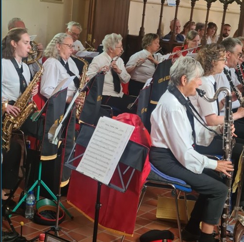 Ely Military Band A band of musicians in white shirts plays woodwind instruments indoors with sheet music stands.